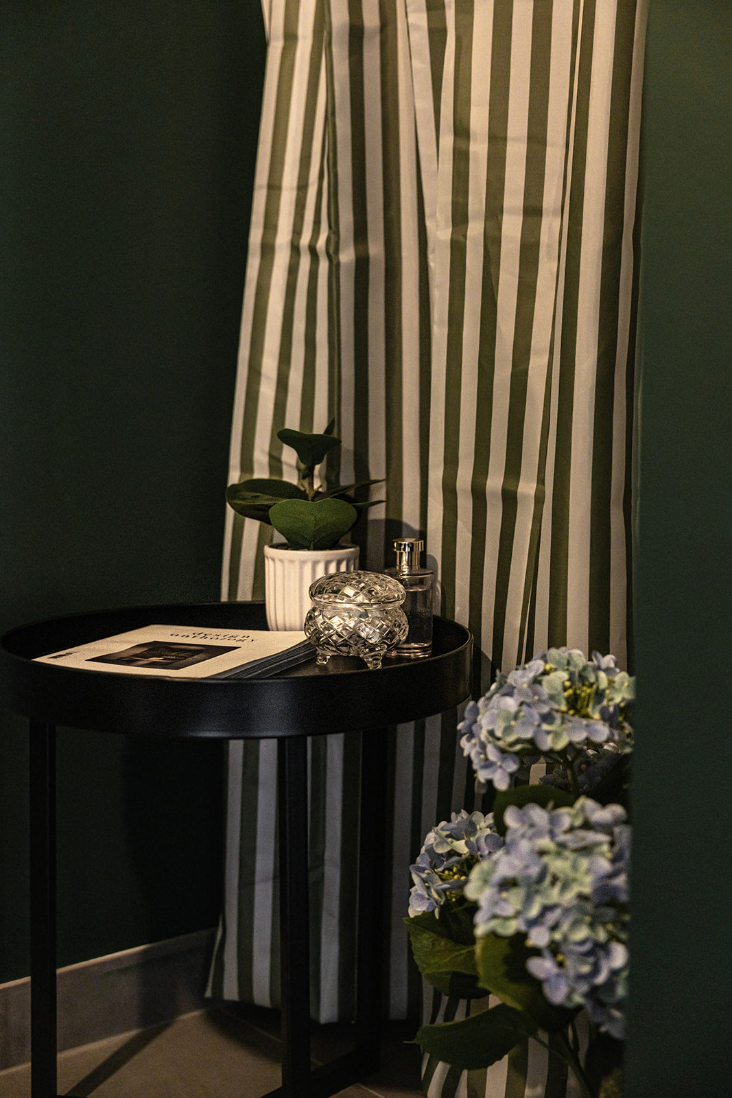 Round black table with decorative items against a dark wall with striped curtains.