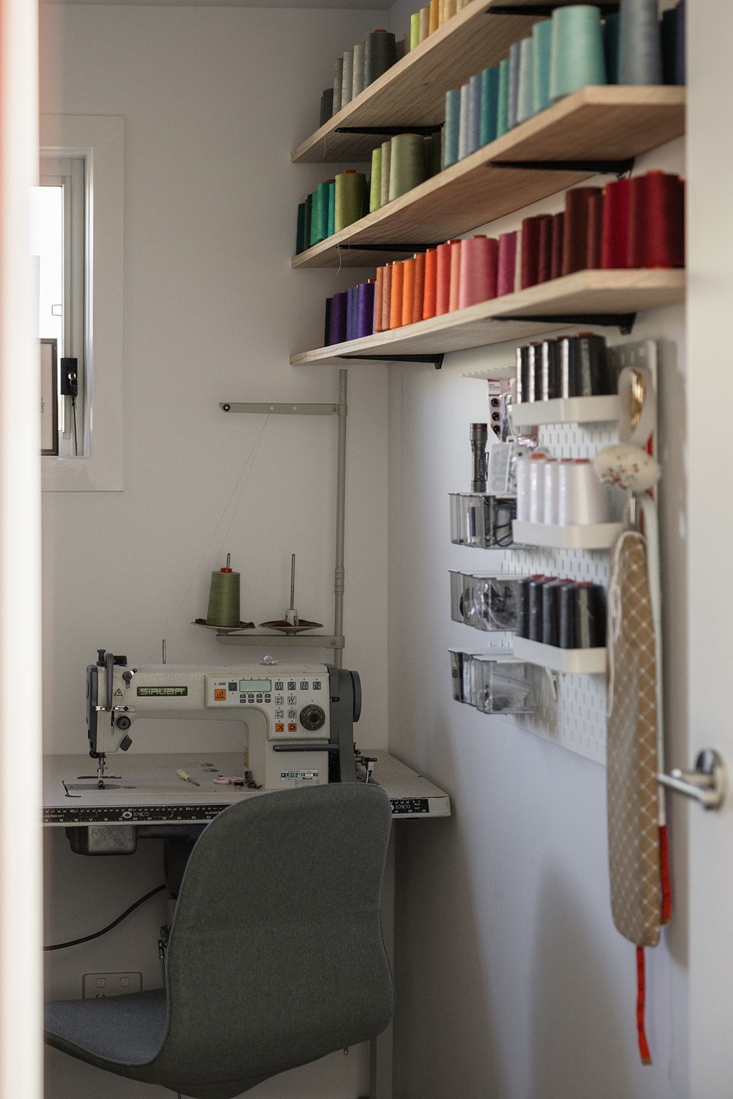 Small office or craft room with sewing machine, colorful shelves, and wall-mounted storage.